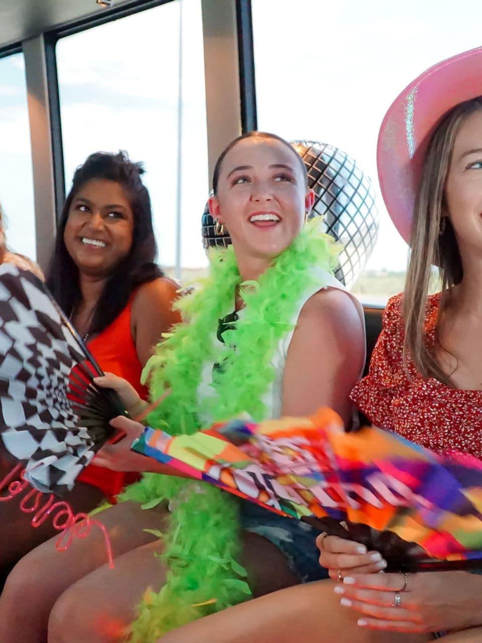Four women smiling on a party bus, holding flags and boas