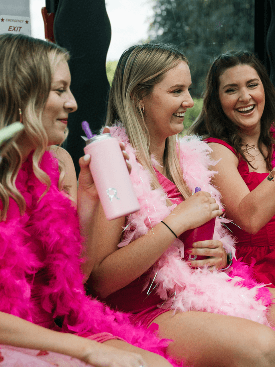 Four friends laughing in a party bus, wearing pink boas and holding drinks.
